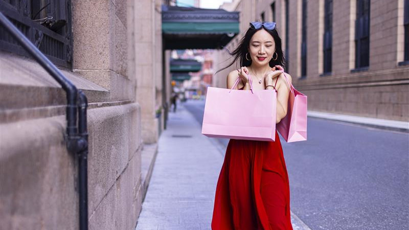 A woman in a red dress stands holding several shopping bags, smiling as she enjoys her shopping experience. image