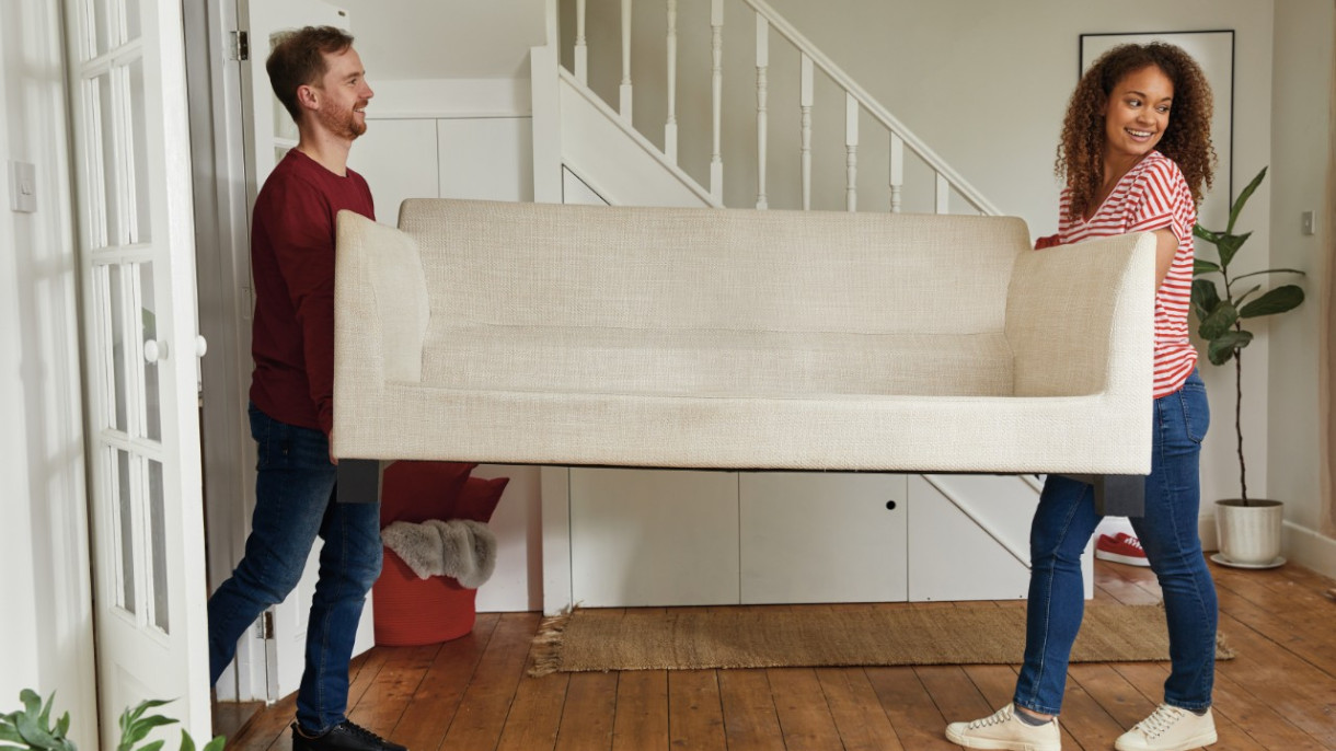 A man and woman are carefully moving a couch into a room together. image