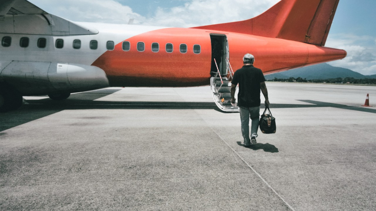 A man walks towards an airplane, pulling luggage behind him on a sunny day at the airport. image