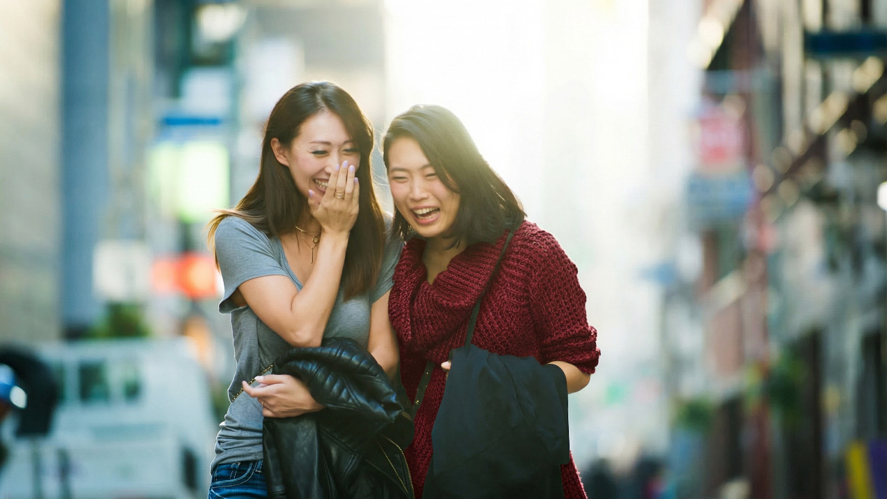 Two women laughing and chatting together on a lively street, enjoying their time outdoors.