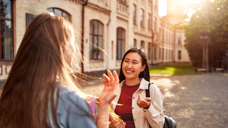Two young women engaged in conversation outside a building, sharing ideas and experiences in an educational setting.