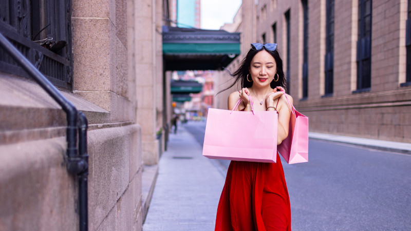 A stylish woman carries shopping bags, enjoying her time in a lively city setting.