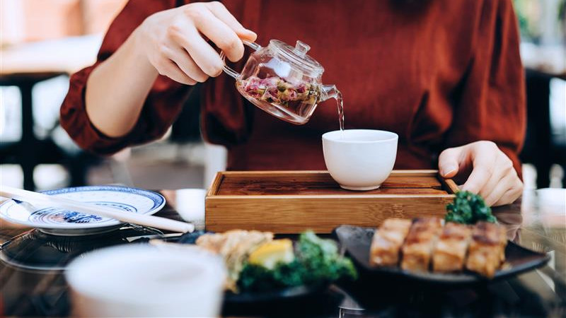 A woman gracefully pours tea from a teapot into a delicate cup.