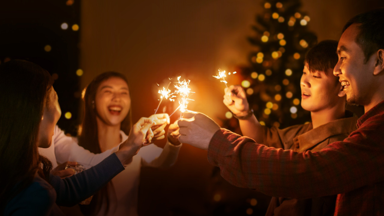 A group of people joyfully holding sparklers in front of a beautifully decorated Christmas tree.