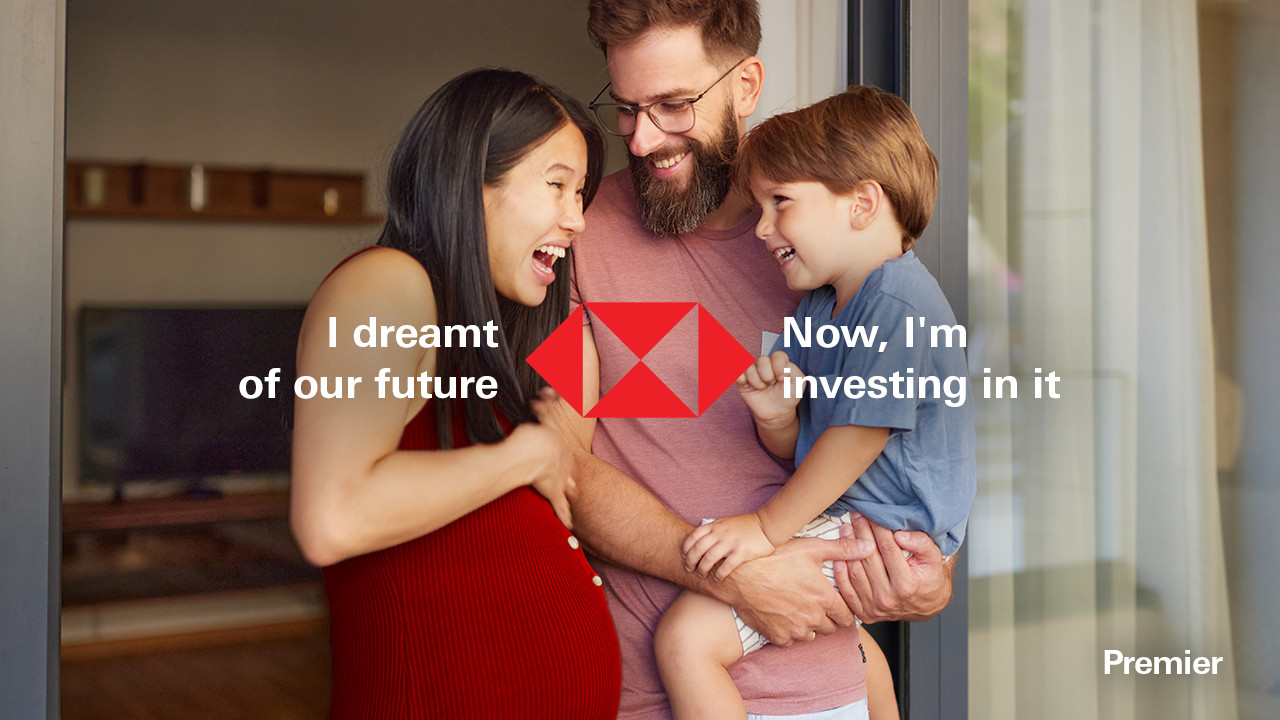 A man, woman, and child stand together in front of a glass door, smiling and looking towards the camera.